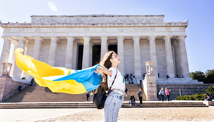 A young woman in front of the Lincoln Memorial drapes a Ukrainian flag in the wind behind her.