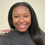 Kennedi Wilson standing in a gray shirt and smiling.