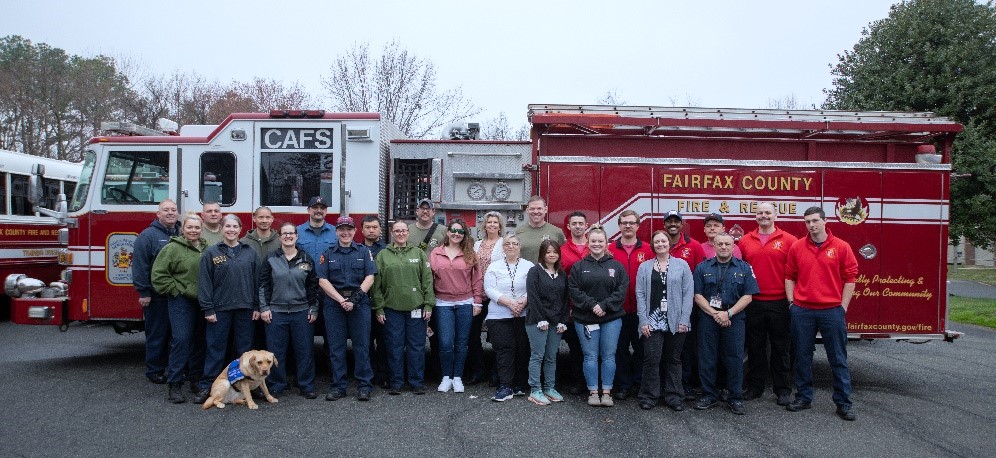 A group of people and a dog stand smiling in front of a fire engine
