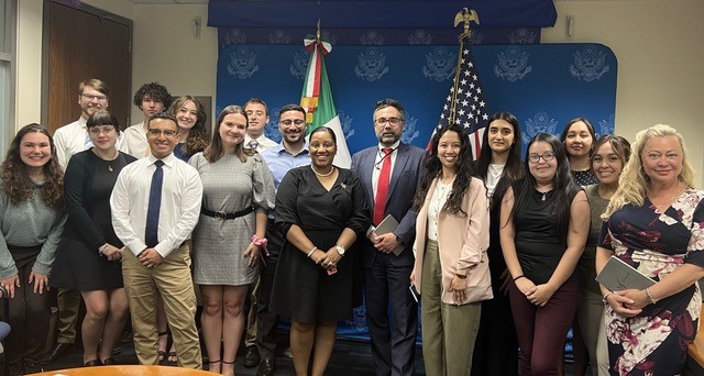A group of people stand in front of a red, white, and blue sign of the number 200.