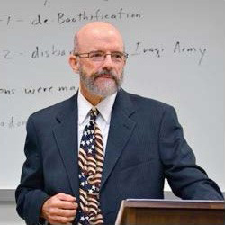 Jim Pfiffner stands in a gray suit with a white collared shirt and American flag tie
