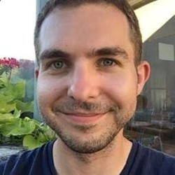 A man in a black shirt stands outside and smiles