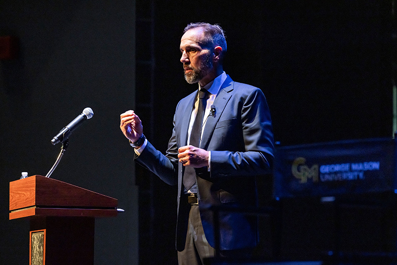 A man in a blue suit jacket stands in front of a microphone.
