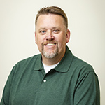 A man in a green collared shirt stands and smiles