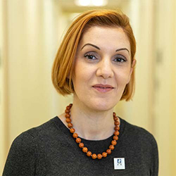 A woman wearing a black shirt and a brown necklace stands in a hall and smiles