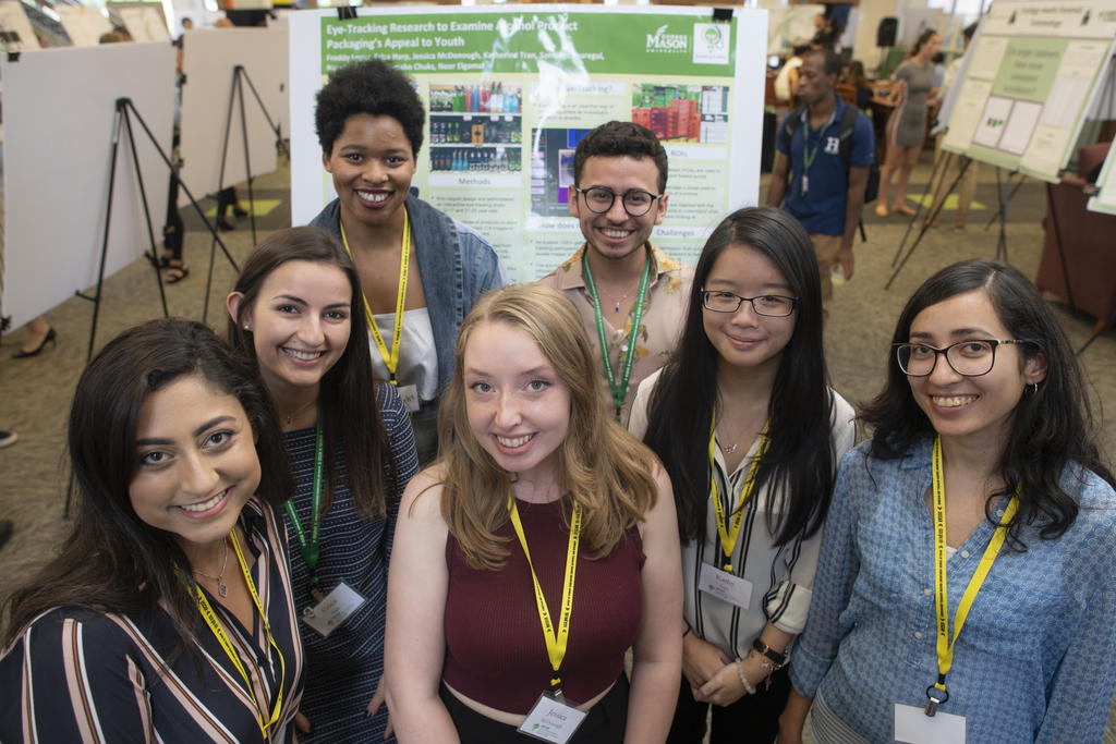 A group of George Mason University OSCAR students in front of a research project board