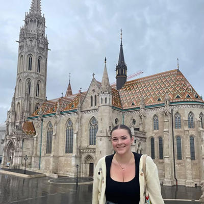 Schar School junior Maggie Reier sitting and smiling in front of a building in Budapest