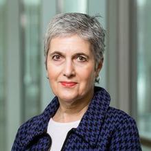 A woman with short gray hair wearing a blue checked jacket poses for the camera.