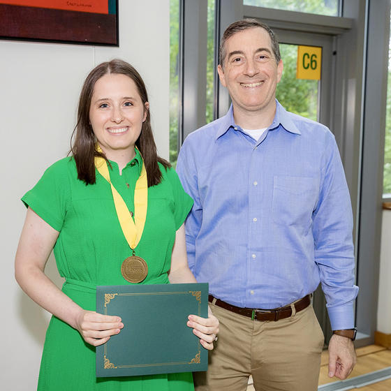 A woman in a green dress wearing a medal stands next to a smiling man in a blue shirt.