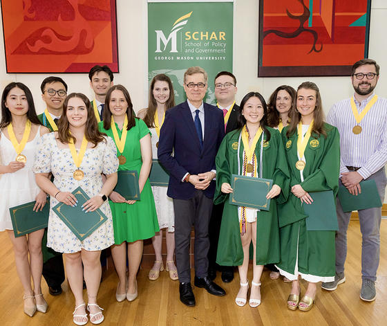 A man in a blue suit stands with 11 men and women, some of them holding certificates in folders.