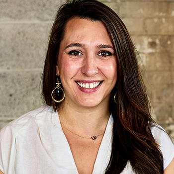 A woman with dark hair and a white top smiles at the camera.