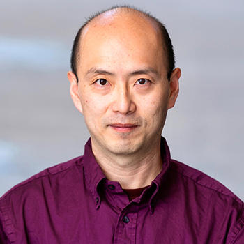 A man in a purple shirt gazes at the camera.