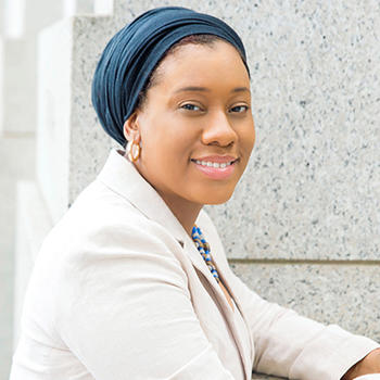 A woman in a white jacket and a blue head scarf smiles at the camera.