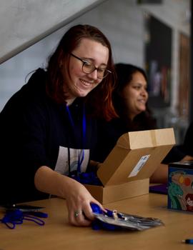 A young woman opens a box on a table.