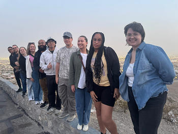 Ten individuals stand on a low stone wall and pose for the camera.