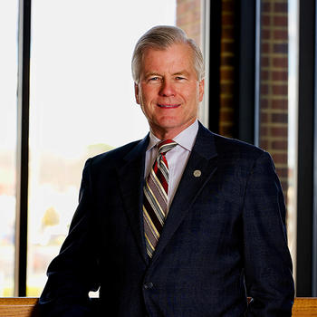 A man in a dark suit jacket and striped necktie smiles at the camera.