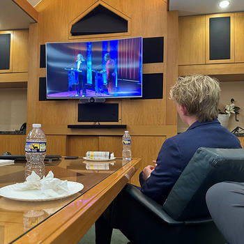 A person in a blue jacket looks at a TV screen.